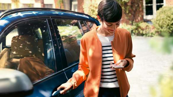 Una mujer mira su smartphone y abre la puerta de su BMW BMW TeleServices Mujer mira su smartphone y abre la puerta de su BMW